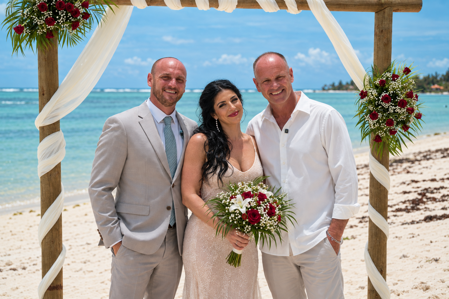 Portrait des mariés avec leur maître de cérémonie sous l’arche de plage